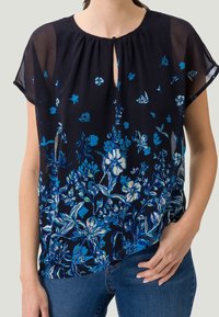 Blouse marine avec un motif floral dans des nuances de bleu, décolleté en forme de clé, manches courtes et coupe ample, réalisée en tissu léger.