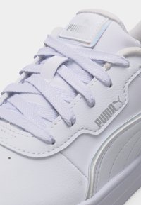 Λευκό αθλητικό παπούτσι Puma με λευκά κορδόνια, ορατό λογότυπο στη γλώσσα και την πλευρά, και ελαφρώς υφή δερμάτινο επάνω μέρος σε κοντινή λήψη.