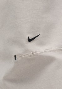 Φωτεινό μπεζ ύφασμα με μικρό μαύρο λογότυπο Nike swoosh και οριζόντια ραμμένη ραφή από κάτω.