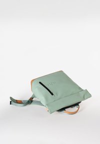 Muntgroene rugzak met tan accenten, verstelbare schouderbanden, een frontzak met ritssluiting en een oprolbare sluiting. Gladde textuur, modern ontwerp.