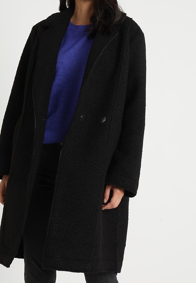 Černý, texturovaný kabát s rovnými liniemi. Obsahuje límec a dva přední knoflíky, nošený přes modrý svetr a černé kalhoty.