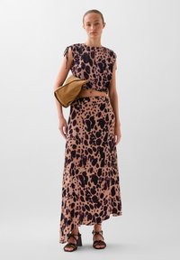 Maxi jurk met een luipaardprint in beige en donkerbruin. Beschikt over korte mouwen, een cropped top en een losse pasvorm. Geaccentueerd met een bruine tas.