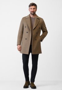 Brauner Woll-Peacoat mit doppelter Knopfleiste, großen schwarzen Knöpfen und Reverskragen. Getragen über einem beigen Pullover und schwarzen Slim-Fit-Hosen.