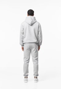 Sivi komplet trenirke s kapuljačom i hlačama od mekog pamučnog materijala. Kapuljača ima veliki stražnji džep i rebraste manžete; uparena s odgovarajućim joggericama.