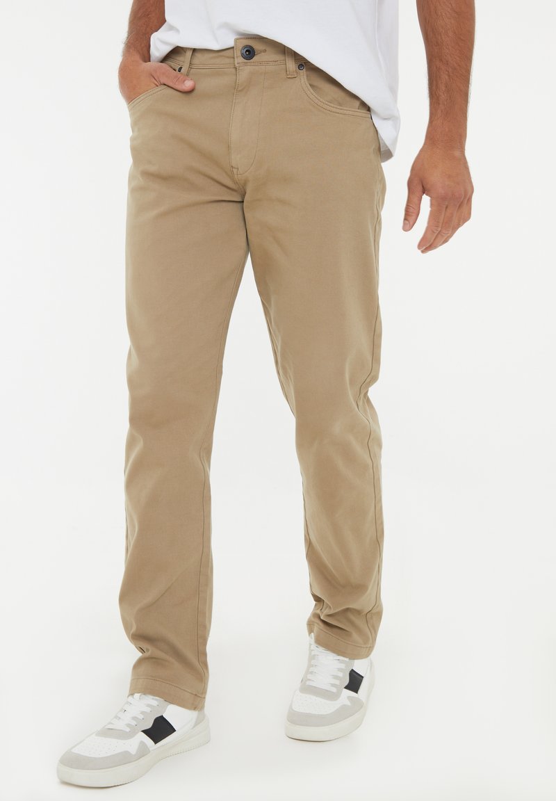 Beige Baumwollmischungshosen mit geradem Schnitt, Fronttaschen und Knopfverschluss. Kombiniert mit weißen Sneakers mit schwarzen Akzenten.