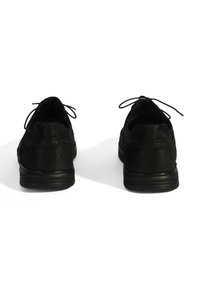 Chaussures en cuir noir présentant un bout arrondi, un extérieur texturé et des lacets fins. La semelle est légèrement surélevée avec des rainures horizontales.