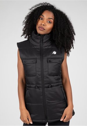 Zwarte gewatteerde vest met hoge kraag, ritssluiting en twee voorzakken. Voorzien van een trekkoord in de taille en een logo op de borst.