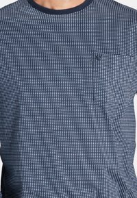 Marineblaue T-Shirt mit strukturiertem Quadratmuster, Rundhalsausschnitt und Brusttasche. Hergestellt aus weichem Material, mit kurzen Ärmeln.