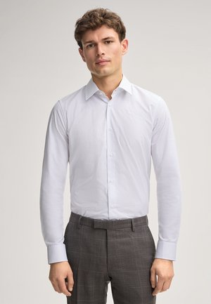 Chemise blanche à manches longues avec une texture subtile, boutonnière à l'avant et col classique, associée à un pantalon à carreaux gris à façade plate.