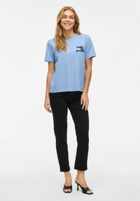 Ljusblå bomullströja med texten "Njut av processen" i svart, tillsammans med svarta byxor och svarta öppna klackar.