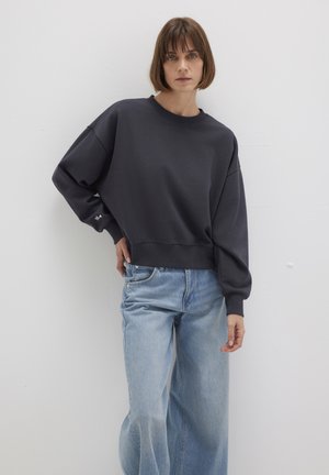 Dunkelgrauer Sweatshirt mit Rundhalsausschnitt und überschnittenen Schultern, kombiniert mit hellblauen weit geschnittenen Jeans. Schlichtes und unaufdringliches Design.