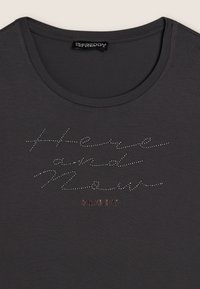 T-shirt grigia con collo rotondo, caratterizzata da lettere in strass che recitano "Here and Now" e il nome del marchio "FREDDY" in rosso.