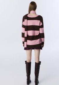 Fuzzy roze en bruine gestreepte trui met een ontspannen pasvorm, gecombineerd met een donkere rok en elegante bruine kniehoge laarzen.