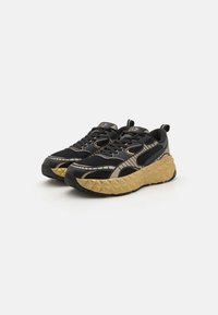 Mustan ja kullan värinen tekstuurilla varustettu sneaker, jossa on verkkoyläosa, tukeva geometrinen pohja ja voimakas nauhakiinnitys varmistaen mukavan istuvuuden.