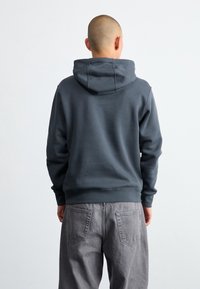 Mörkgrå, hooded sweatshirt i texturerad tyg. Har ribbade ärmslut och nederkant. Matchad med ljusgrå, avslappnade byxor, uppvisar bakvy.