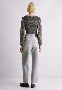 Cvećasti top s dugim rukavima i prozirnim rukavima, uparen sa svijetlosivim trapericama visokog struka i crnim ravnim cipelama. Jednostavan dizajn.