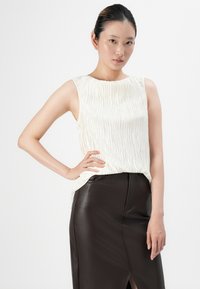 Weißes, plissiertes, ärmelloses Top mit rundem Halsausschnitt, kombiniert mit einem figurbetonten, dunklen Ledrock mit einem vorderen Schlitz. Glatte Textur, minimalistisches Design.