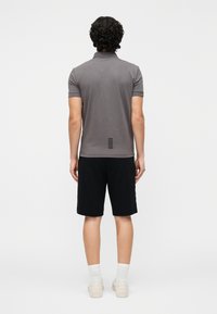 Grå polo-shirt med et diskret mønster på ryggen, kombineret med sorte shorts. Modellen vender ryggen til. Sneakers og hvide sokker er synlige.