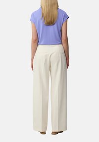 Lichtpaarse top met korte mouwen en een ronde hals, gecombineerd met losse witte wijde broek met achterzakken, gedragen met beige sandalen.