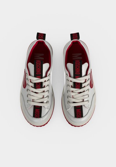 Ζευγάρι λευκά και κόκκινα sneakers Moschino με λευκά κορδόνια, μαύρη και κόκκινη λωρίδα λογότυπου στη γλώσσα και κόκκινη εσωτερική επένδυση.