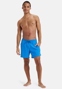 Modré plavky vyrobené z ľahkého materiálu, s elastickým pásom so šnúrkou, bočnými vreckami a akcentom loga.