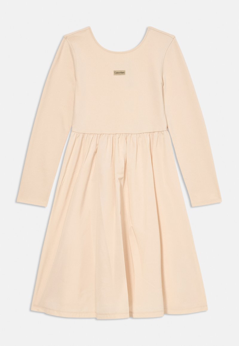 Vestido de mangas longas em tecido pêssego claro com corpete ajustado e saia rodada. Apresenta um pequeno logótipo da Calvin Klein no peito.