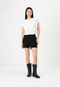 T-shirt blanc à œillets à manches courtes associé à un short noir ajusté et des bottes noires jusqu'aux genoux avec une boucle. Design minimaliste, couleurs nettes.