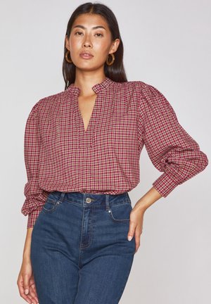 Rot-beige karierte Bluse mit Stehkragen und puffigen Ärmeln, kombiniert mit hochtaillierten blauen Jeans.