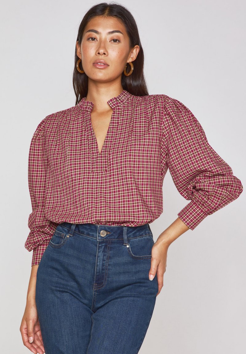 Blusa a scacchi rossa e beige con colletto alla mandarina e maniche a palloncino, abbinata a jeans in denim blu a vita alta.