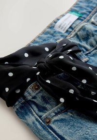 Džínsy z denimu s čiernou šatkou s bodkami previazanou okolo pása. Šatka dodáva outfitu kontrastnú textúru a vzor.