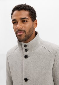 Cappotto grigio in lana con colletto alto, dotato di tre bottoni neri, design strutturato e finitura morbida e testurizzata.