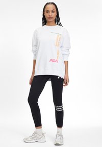Felpa bianca oversize con testo stampato colorato; abbinata a leggings neri con testi e dettagli bianchi; sneakers chiare.