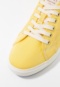 Gul canvas sneakers med ribbad textur, vit gummisula och vita snören. Har metallöglor och stygnaccent.