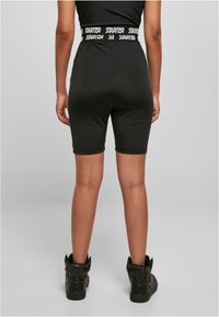Shorts de cyclisme noirs avec une coupe ajustée et une large taille élastique arborant le texte "STARTER" en blanc. Portés avec des baskets noires montantes.