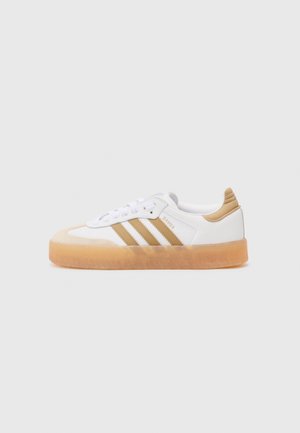 Witte en beige Adidas Samba sneaker met rubberen zool, beige strepen en beige hieltab op een effen lichte achtergrond.