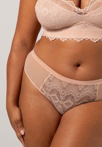 Lingerieset met een kanten bh en bijpassende slip in lichtroze. De bh heeft een gegolfde rand, en de slip combineert doorschijnend materiaal met kantdetails.