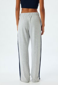 Lichtgrijze sweatpants met marineblauwe zijkanten, gemaakt van zacht materiaal. Heeft een elastische tailleband en een taps toelopend ontwerp.