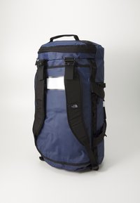 Navy blue backpack with black straps, reflective patch, and zipper closure. Features a cylindrical shape and reinforced carrying handles.