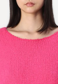 Bright pink knit sweater with a wide neckline and ribbed texture, showing a soft, loose fit. Seamless design with no visible hardware.