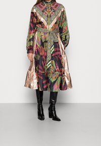 Abito multicolore con una combinazione di motivi floreali e geometrici, colletto alto, maniche lunghe, vita aderente e orlo a balze stratificate.