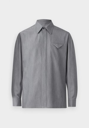 Szürke, hosszú ujjú ing, hegyes gallérral és bal melletti zsebével, amely háromszög alakú fedéllel rendelkezik. Simára szőtt anyag.