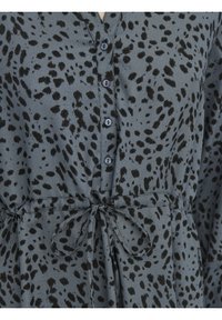 Robe grise avec des taches noires irrégulières, des boutons sur le devant et une ceinture en tissu nouée à la taille.