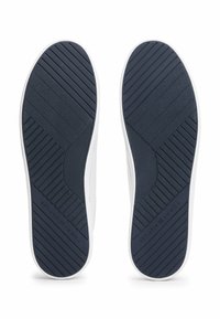 White shoe soles featuring a blue rubber texture with diagonal and horizontal ridges for grip, including a circular accent near the heel.