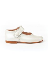 Zapato de piel blanca con punta redondeada, bordes festoneados en la correa y cierre de botón. Suela plana marrón.