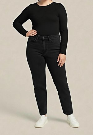 Osoba ubrana w czarną bluzkę z długim rękawem, czarne jeansy z wysokim stanem, białe trampki, stojąca z jedną ręką na biodrze na jednolitym tle.