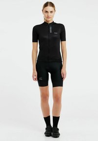 Čierny cyklistický dres s krátkymi rukávmi, predný zips, modré vertikálne pruhy. V páre s čiernymi šortkami s vystužením, tmavými ponožkami a cyklistickými topánkami.
