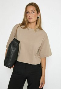 Cropped beige t-shirt with short sleeves, paired with black leather bag. Smooth texture, simple design, no visible patterns or embellishments.