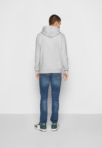 Grå hættetrøje med en stor hætte, ribbede manchetter og kant; parret med blå jeans og grønne høje sneakers. Bagfra set mod en hvid baggrund.