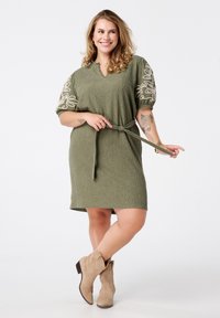 Olijfgroene jurk van een gestructureerde stof, met V-hals, korte pofmouwen met witte bloemenborduursels en een bijpassende strikceintuur.