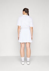 Hvid kortærmet polo-shirt med krave, parret med en flagrende nederdel, begge lavet af letvægtsstof. Fodtøj omfatter hvide sneakers.